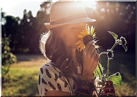 Woman who smells a sunflower, because positive thinking contributes to happiness